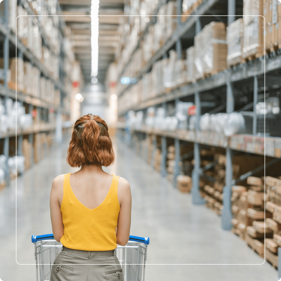 Group 2 (8) A person with a yellow top pushes a shopping cart through a large warehouse aisle lined with shelves filled with various items.