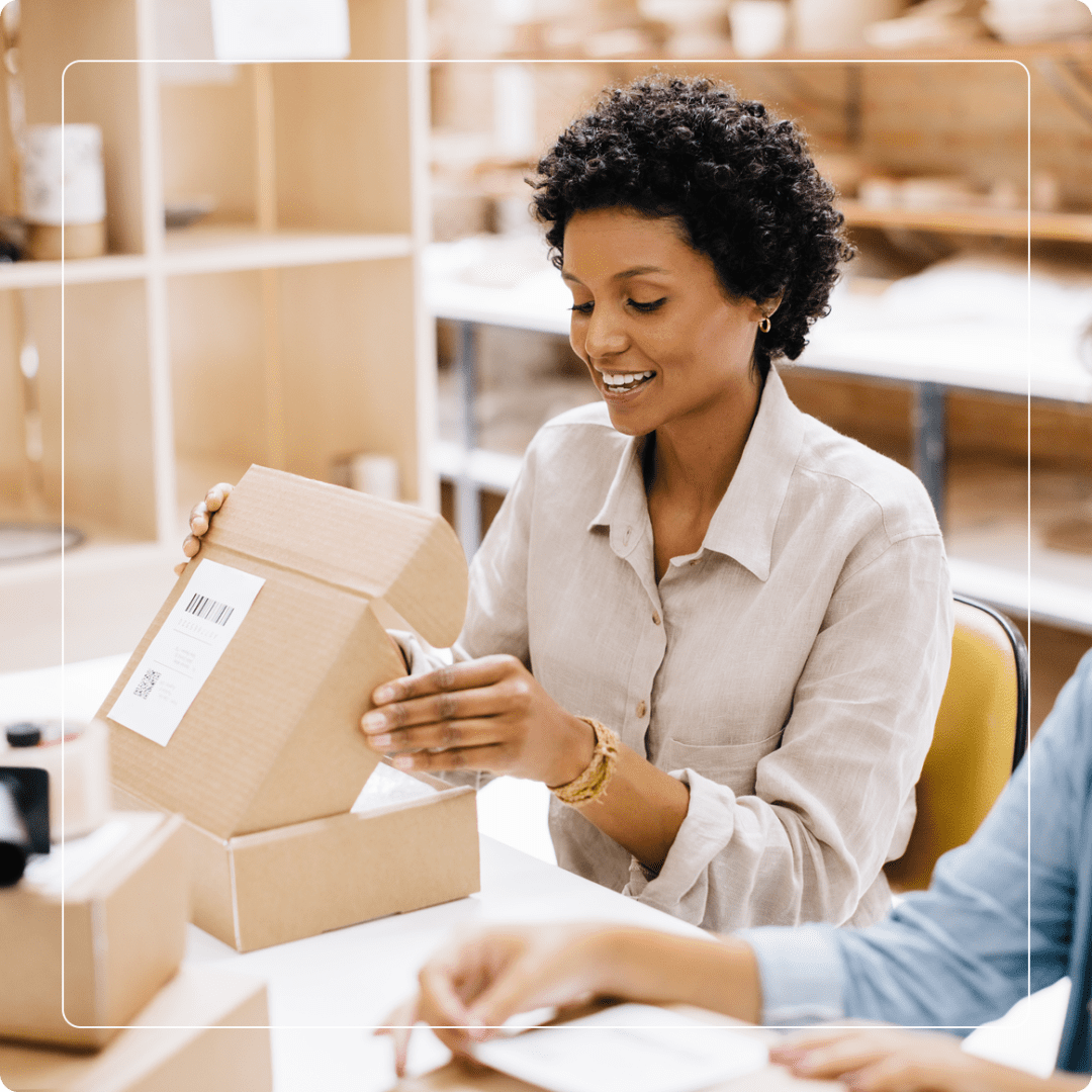 Group 2 (9) A person seated at a table is assembling a cardboard box, surrounded by packaging materials in a workspace.